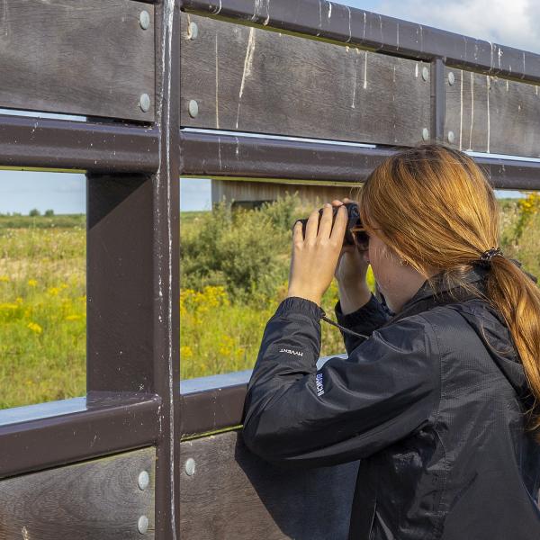 Vrouw kijkt door verrekijker in kijkscherm