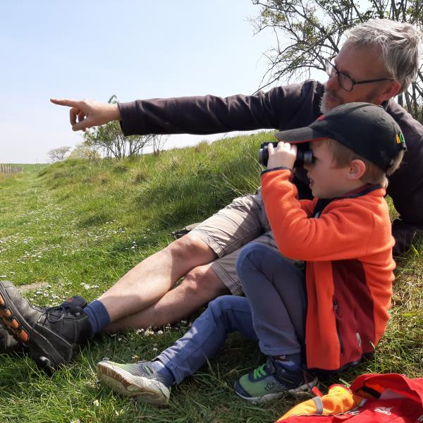 man wijst iets aan in de natuur voor zijn kind die met een verrekijker kijkt