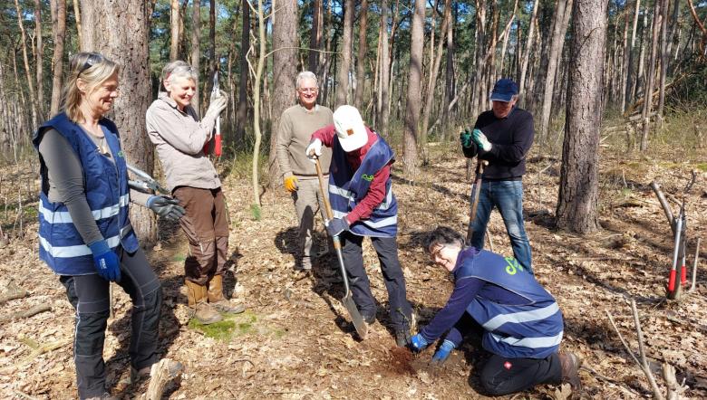 Groep vrijwilligers kijkt naar vrijwilliger die gat in de grond maakt